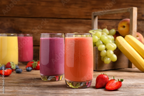 Glasses with different tasty smoothies and ingredients on wooden table