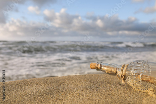 SOS message in glass bottle on sand near sea, closeup. Space for text