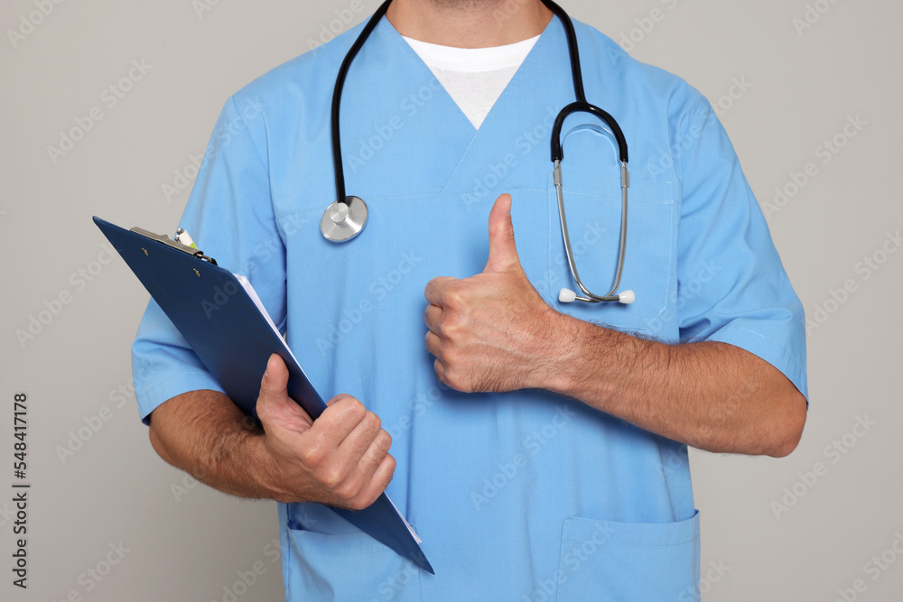 Doctor with stethoscope and clipboard showing thumb up on light grey background, closeup Doctor with stethoscope and clipboard showing thumb up on light grey background, closeup