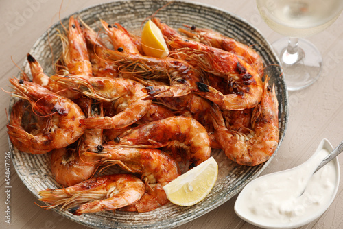 Plate of delicious cooked shrimps served with lemon, sauce and wine at table, closeup