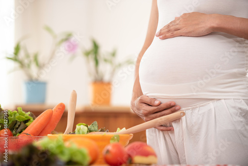 young pregnant woman makes herself salad of fresh vegetables  the concept of proper nutrition. high quality photo. pregnant woman in kitchen making salad.