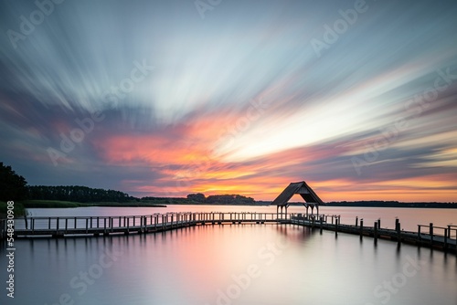 Long exposure shot of a wooden pier in Hemmelsdorfer See under the orange-shaded sunset sky photo