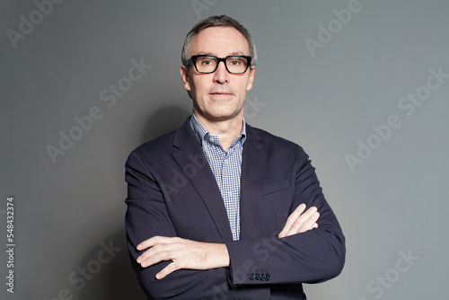 Mature businessman in blue suit and glasses on grey wall background