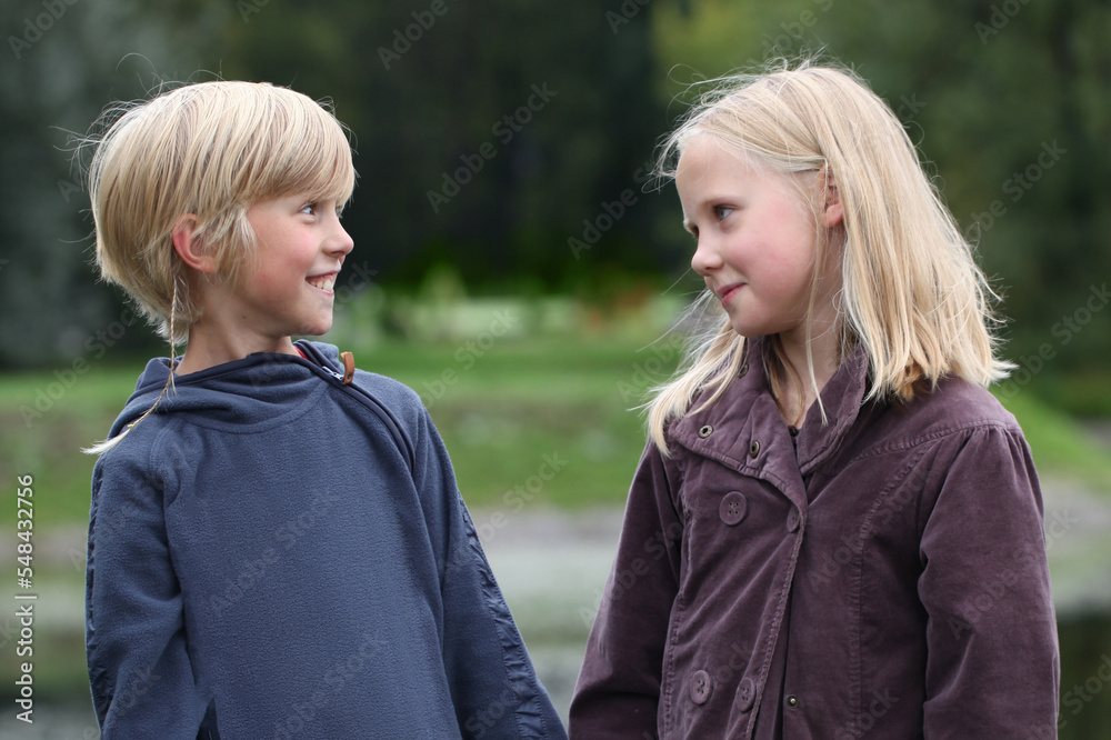 Fototapeta premium Two blonde children little boy and girl are talking in the park outdoors