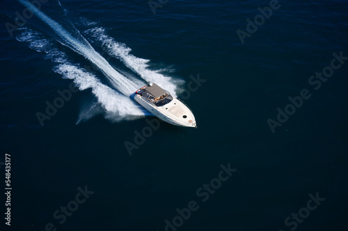 White boat with an awning moving diagonally on dark water top view
