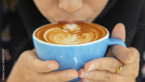 Close up Cup of coffee latte in coffee shop.Female hands holding a cup of coffee cup with flower shaped latte art foam