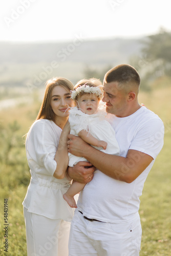 Young family with cute little daughter walking in forest on the sunset
