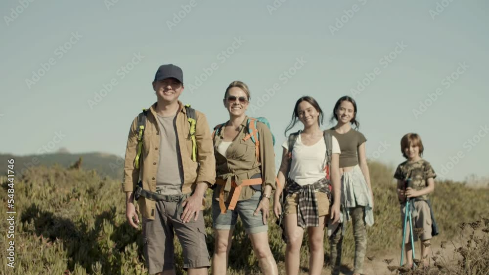 Caucasian family hiking on sunny day, standing in row, smiling. Parents and children posing on footpath, looking happy, enjoying hiking adventure on sunny day. Slow motion. Travel, family concept. Caucasian family hiking on sunny day, standing in row, smiling. Parents and children posing on footpath, looking happy, enjoying hiking adventure on sunny day. Slow motion. Travel, family concept.