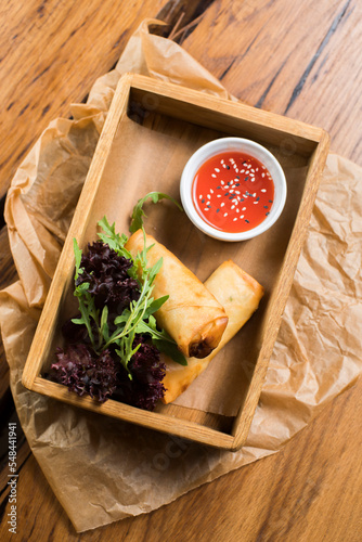 spring rolls serving in a box with herbs and sauce