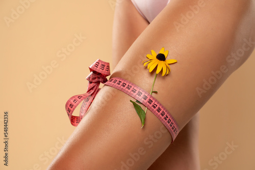 Woman measuring her thigh using a tape measure  isolated on beige background