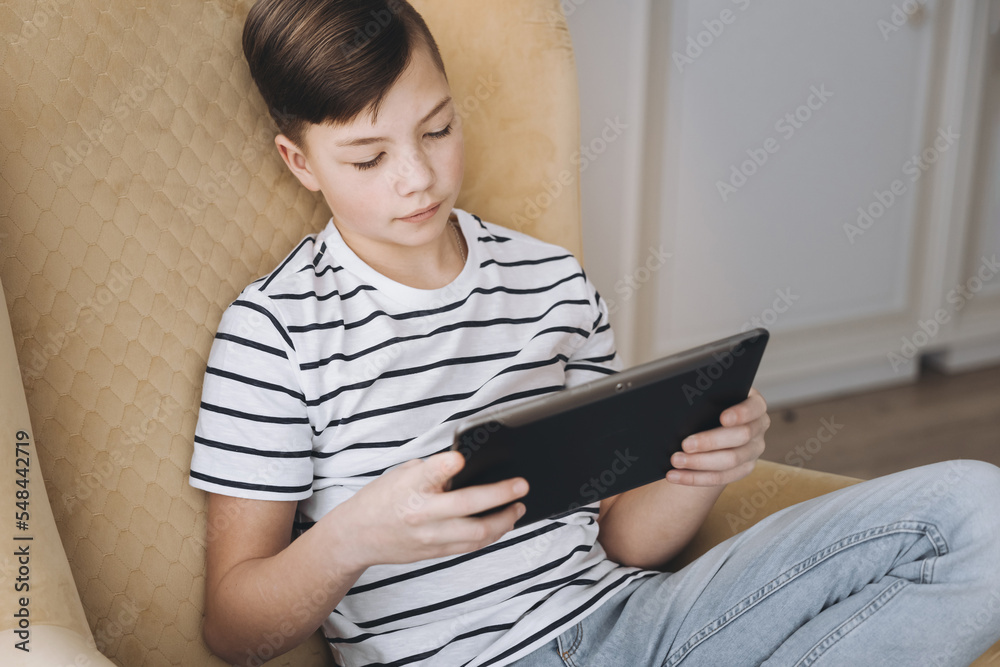 Teenage boy using tablet having video chat on internet online at home. Child watching movie, playing video game. Social media concept. Online education. Distance learning Teenage boy using tablet having video chat on internet online at home. Child watching movie, playing video game. Social media concept. Online education. Distance learning