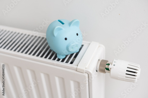 Piggy bank on heating radiator against light background. Space for text.