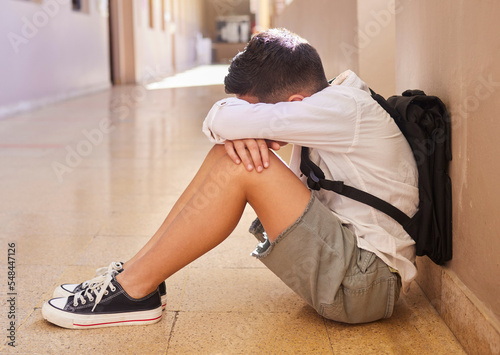 Anxiety, school and sad student bullying victim feeling depression, lost or stressed in hallway or corridor floor. Child, depressed boy or lonely male learner crying alone with abuse trauma or fear