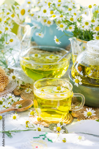 Chamomile herbal tea in a glass cup on wicker coaster on wooden table, healthy chamomile flower drink with honey, fresh chamomile flowers in background, healthcare and healthy eating concept