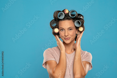 Fotografie Beautiful smiling woman with hair curlers posing on a blue background