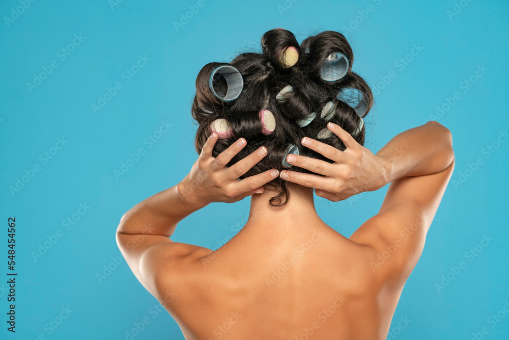 Back view of a young woman with hair curlers and towel posing on a blue background Back view of a young woman with hair curlers and towel posing on a blue background