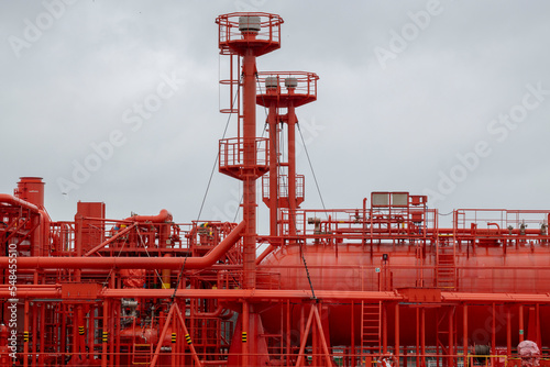 Red cylindrical tanks and pipelines on huge refinery ship with sky in background