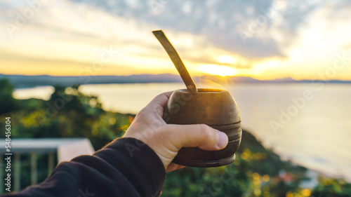 holding a mate cup with beach and mountains background at sunrise