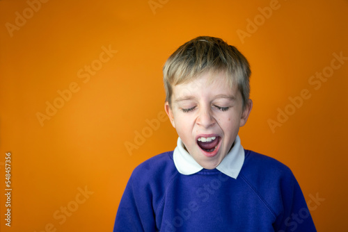 A tired school boy is yawning in school uniform, orange background, copy space