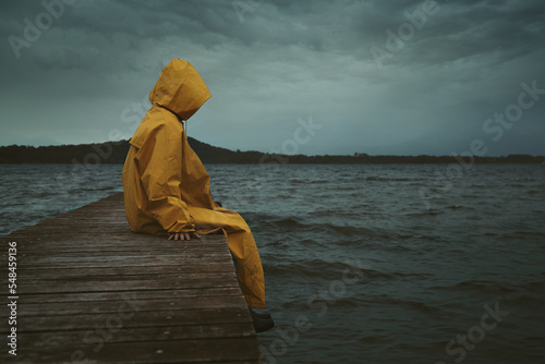Mysterious hooded figure seated on a pier