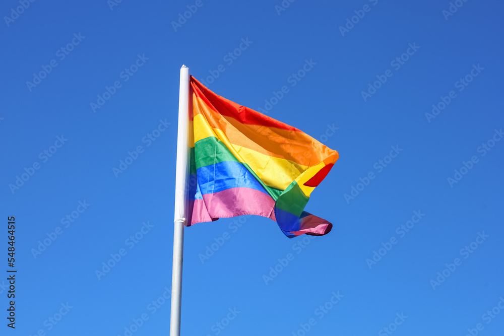 Waving LGBT flag against blue sky Waving LGBT flag against blue sky