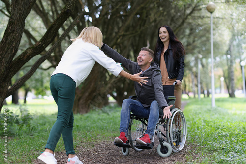 Women friends walking with disabled man in wheelchair in park, happy to see each other