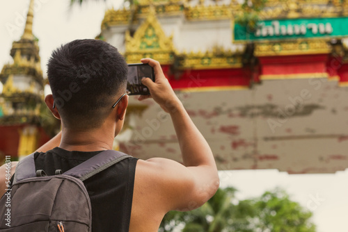 Close up on back of young man taking photos with cellphone of Buddhist temple in Phuket. Male tourist visiting religious building in Thailand. Backpacker in South East Asia concept