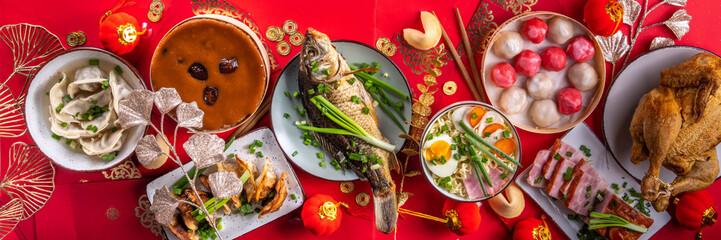 Traditional Chinese lunar New Year dinner table, party invitation, menu background with pork, fried fish, chicken, rice balls, dumplings, fortune cookie, nian gao cake, noodles, chinese decorations