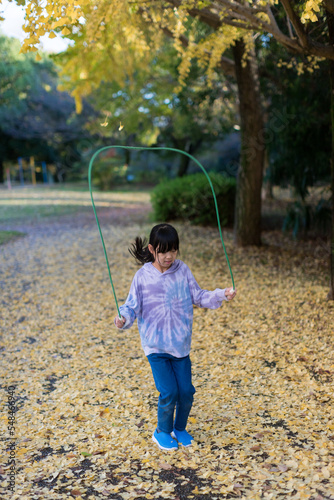 秋の公園で縄跳びをしている小学生の女の子の姿と黄色い銀杏の落ち葉の風景