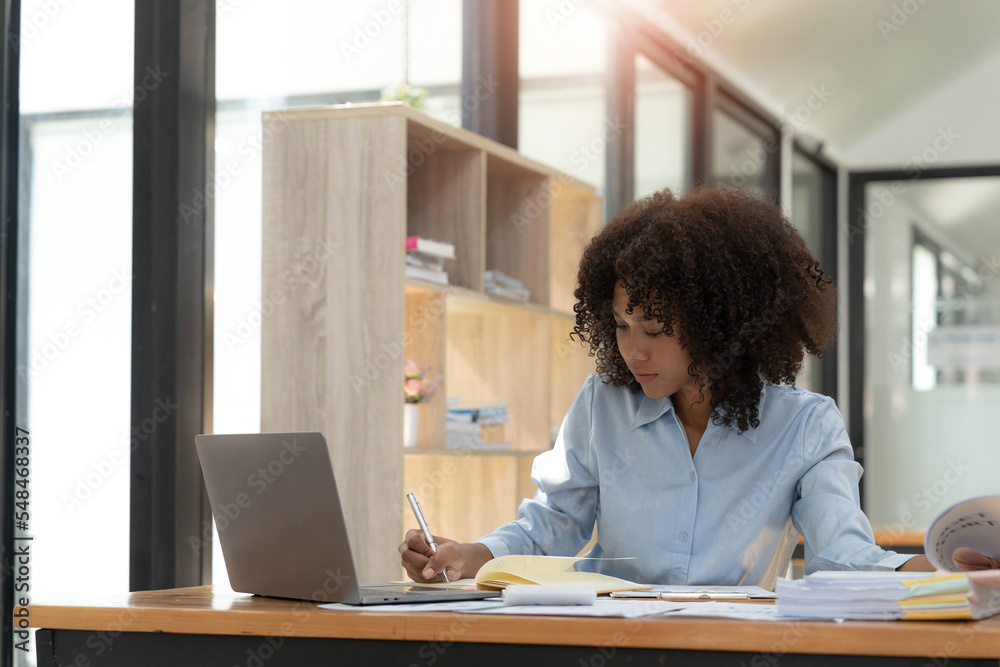 Smiling young African female entrepreneur sitting at a desk in her home office working online with a laptop Smiling young African female entrepreneur sitting at a desk in her home office working online with a laptop