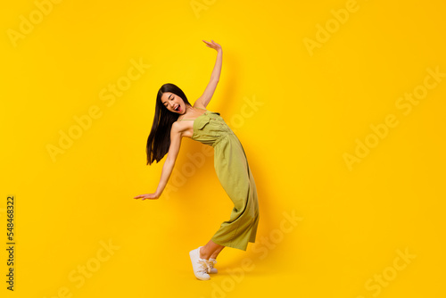 Full body portrait of satisfied glad malaysian lady standing tiptoe dance isolated on yellow color background