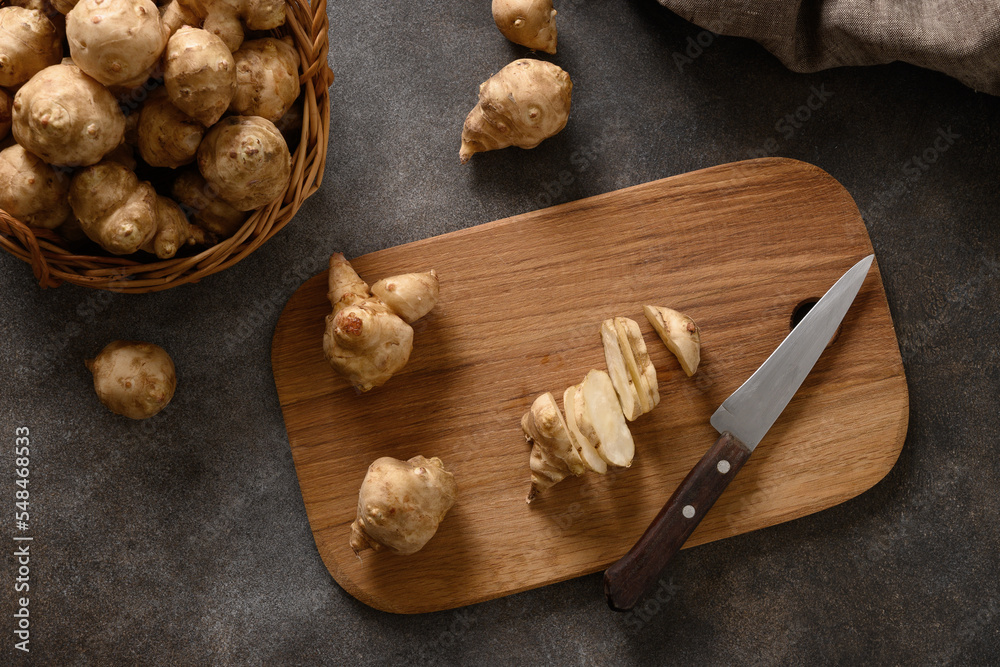 Fototapeta premium Cooking Jerusalem artichoke root, sunchoke on wooden cutting board. Close up. Top view.