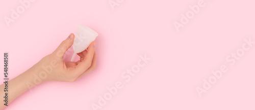 Banner with female hand hold white menstrual cup on a pink background. Minimal concept with place for text. Selective focus.