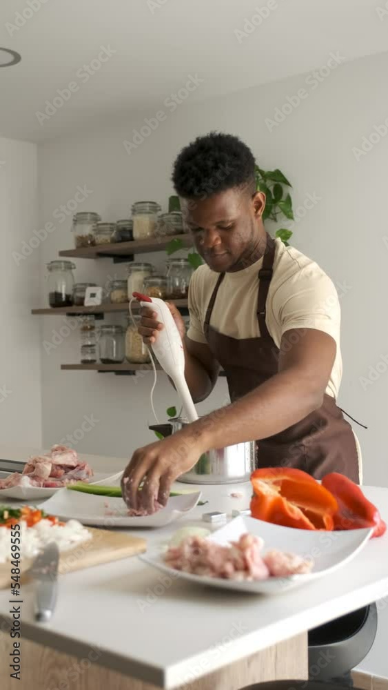 Young black man using a blender to prepare chicken mince in a kitchen. Young black man using a blender to prepare chicken mince in a kitchen.