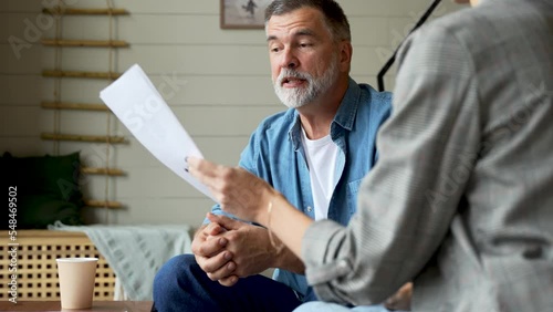 Serious senior mature couple talking disputing holding paper bills checking finances expenses, older middle aged family reading bank loan payments documents at home worried about debt money problems