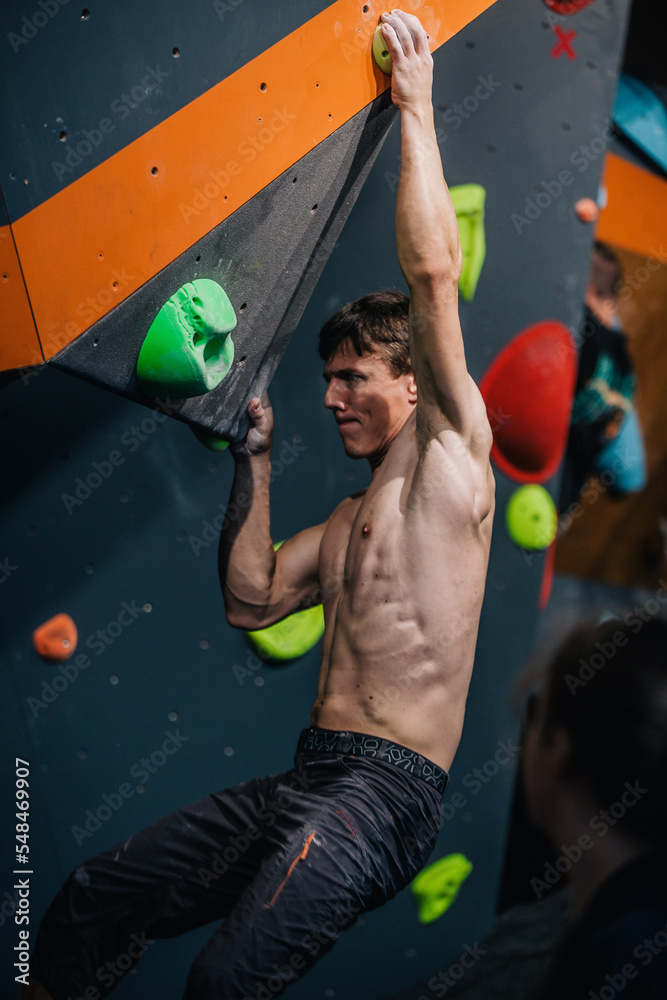 Fototapeta premium A young, athletic guy with a beautiful inflated body climbs a bouldering in a climbing hall. Emotions on the face.