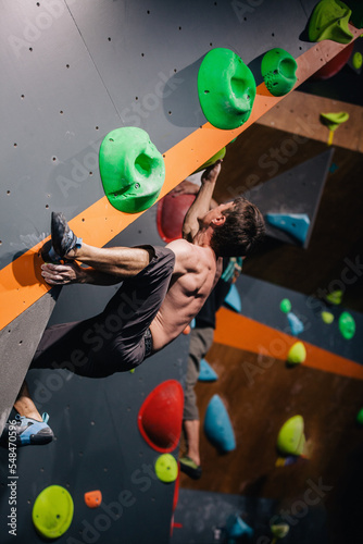 A young, athletic guy with a beautiful inflated body climbs a bouldering in a climbing hall. Emotions on the face.