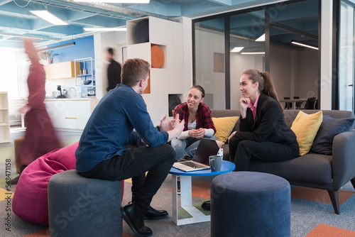 Multiethnic startup business team on meeting in a modern bright open space coworking office. Brainstorming, working on laptop. Group of coworkers walking around in motion blur.