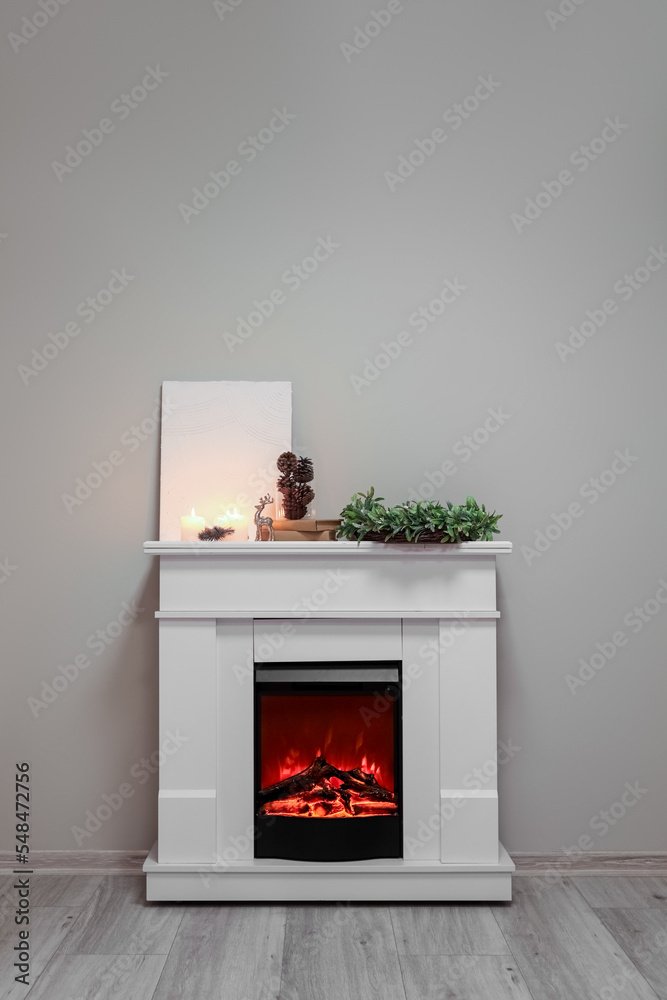 Blank poster with candles, Christmas wreath, fir cones and books on fireplace near grey wall Blank poster with candles, Christmas wreath, fir cones and books on fireplace near grey wall