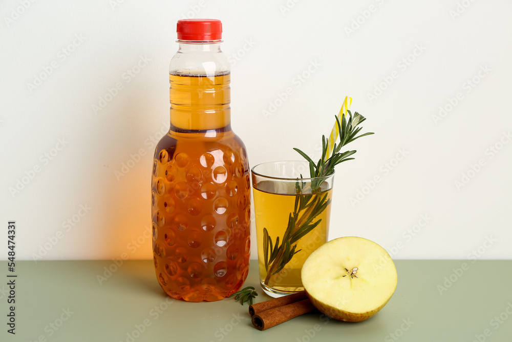 Bottle and glass of fresh apple juice with rosemary on color table Bottle and glass of fresh apple juice with rosemary on color table