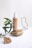 A composition of wire, stones and natural cosmetic bottle of cream balancing on beige color pebble.