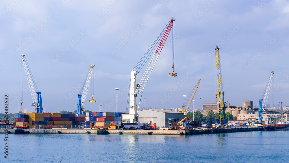 cargo sea port with cranes, container stacks and trucks with goods, sea hub terminal from seashore