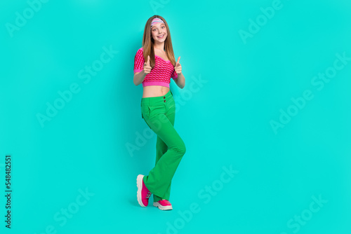 Fototapeta Naklejka Na Ścianę i Meble -  Full length photo of adorable excited schoolgirl wear pink crop top flared pants pointing finger you empty space isolated turquoise color background