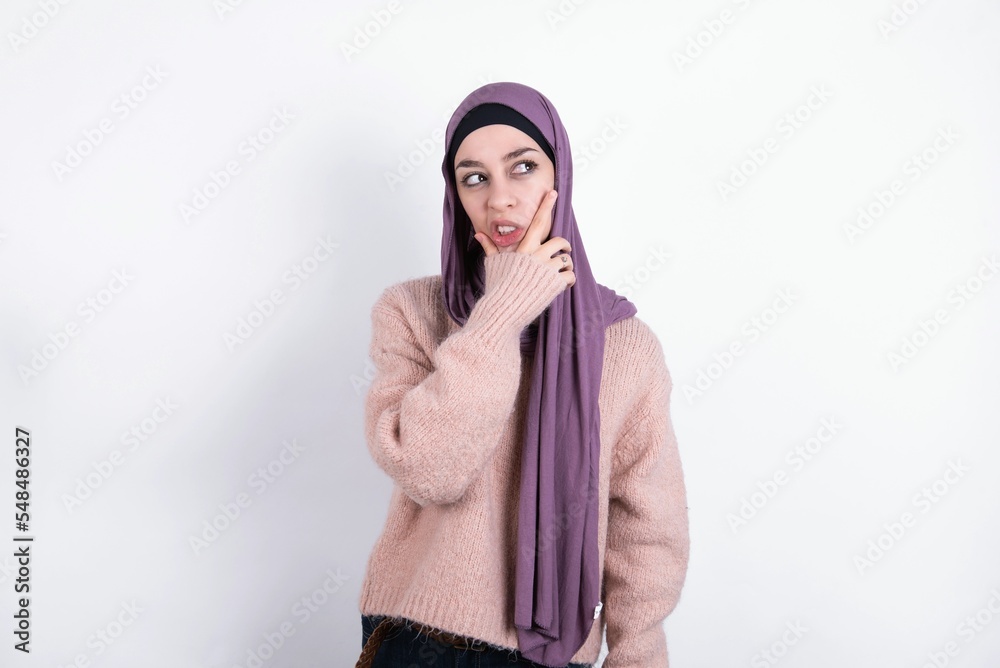 muslim woman wearing hijab and knitted sweater over white background Thinking worried about a question, concerned and nervous with hand on chin.