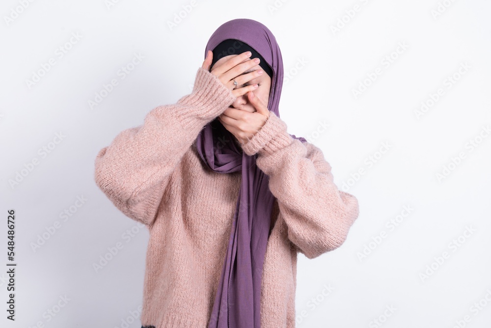Εκτύπωση καμβά muslim woman wearing hijab and knitted sweater over white background Covering eyes and mouth with hands, surprised and shocked
