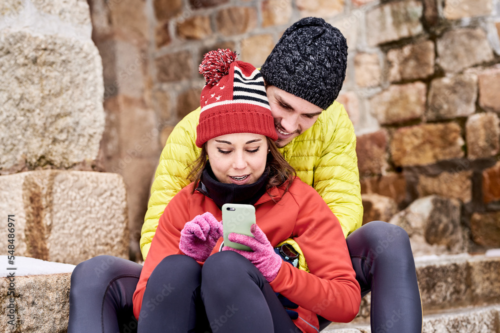 Couple using smartphone together in winter Couple using smartphone together in winter