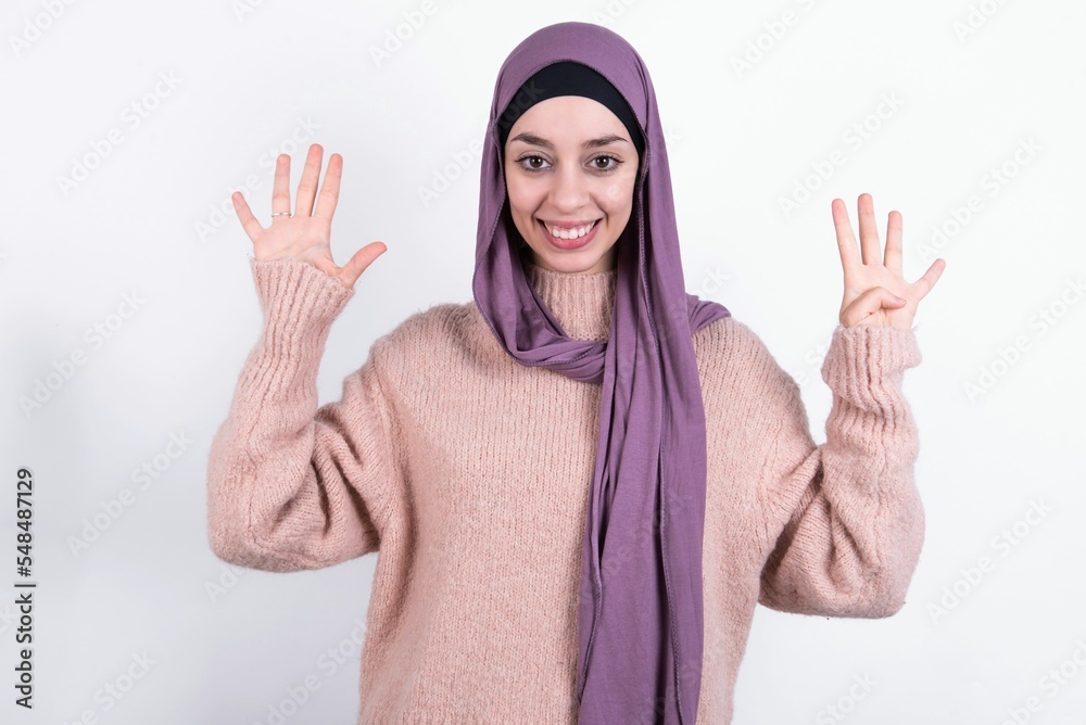 beautiful muslim woman wearing hijab and warm jumper over white background showing and pointing up with fingers number nine while smiling confident and happy.