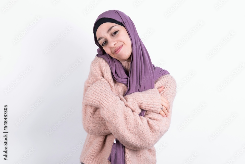beautiful muslim woman wearing hijab and warm jumper over white background Hugging oneself happy and positive, smiling confident. Self love and self care beautiful muslim woman wearing hijab and warm jumper over white background Hugging oneself happy and positive, smiling confident. Self love and self care