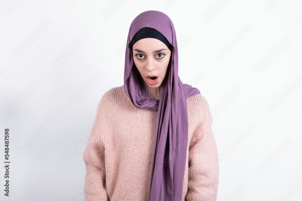 Oh my God. Surprised beautiful muslim woman wearing hijab and warm jumper over white background stares at camera with shocked expression exclaims with unexpectedness, Oh my God. Surprised beautiful muslim woman wearing hijab and warm jumper over white background stares at camera with shocked expression exclaims with unexpectedness,