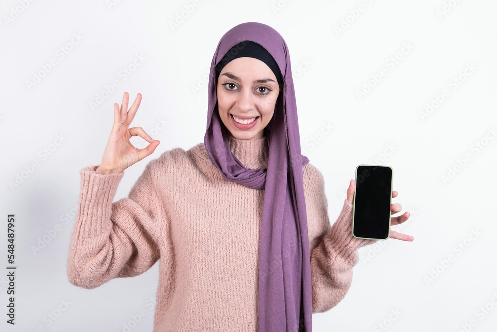 Φωτογραφία beautiful muslim woman wearing hijab and warm jumper over white background holdi